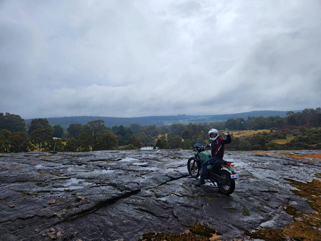 Rex Havoc sitting astride a motorcycle perched on a rock  with Perth in the background